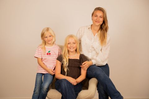 En kvinde og to piger sidder samlet i en lænestol foran en lys baggrund